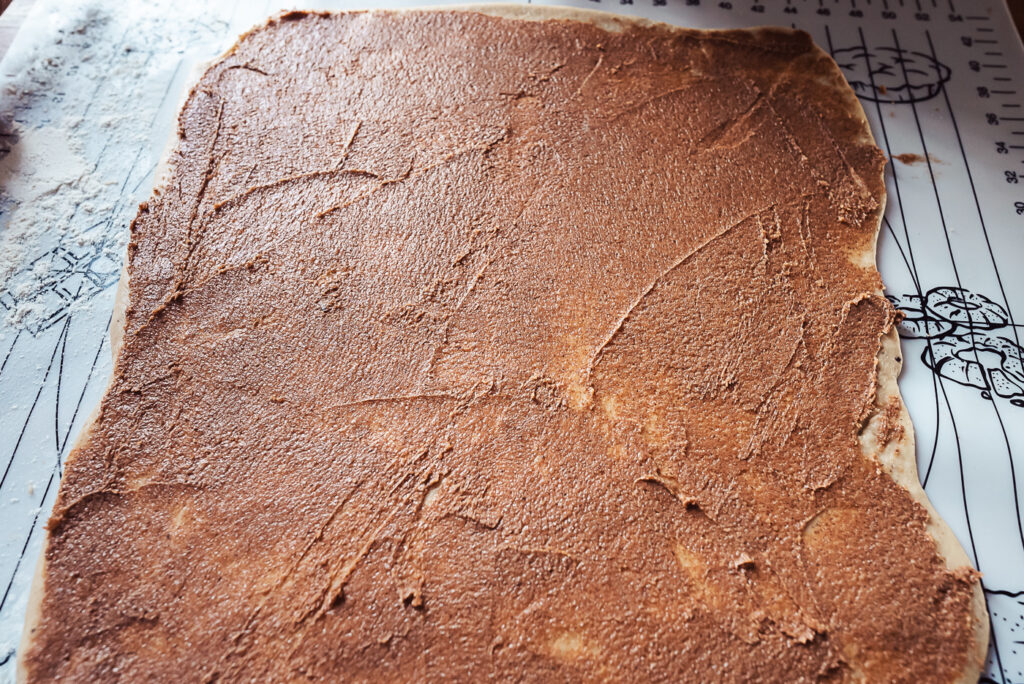 spreading cinnamon sugar on cinnamon bun dough