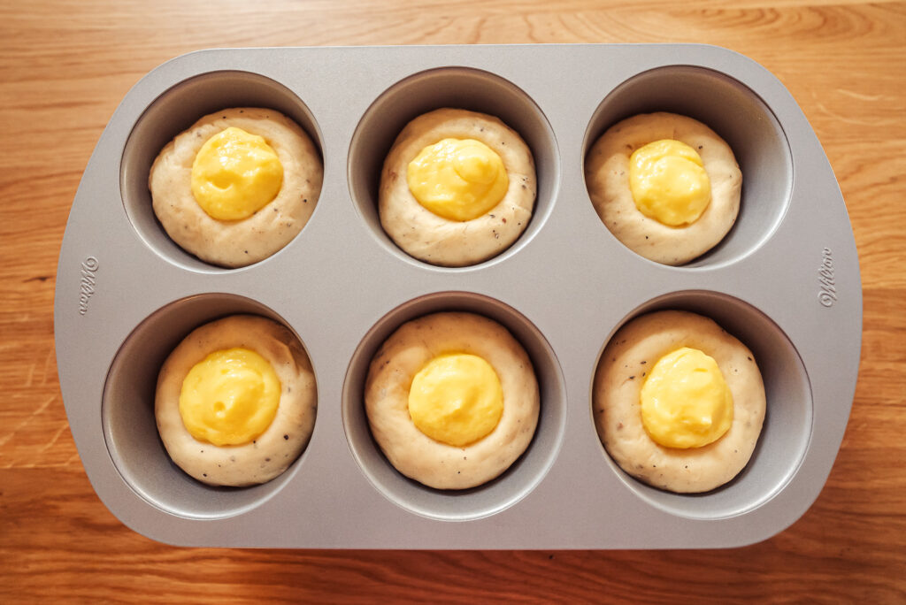 Norwegian skoleboller dough filled with custard and rising in a muffin form