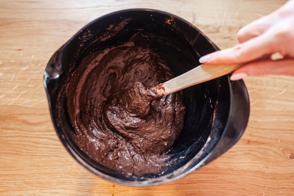 stirring kladdkaka batter in a large black mixing bowl