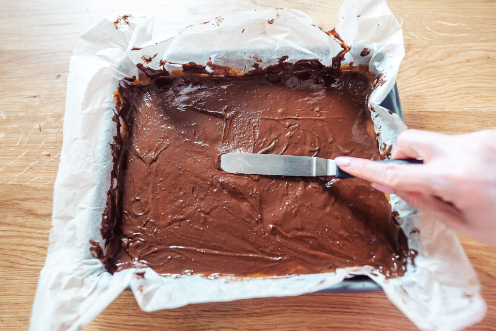 spreading dark chocolate across the top of Norwegian brown cheese caramel squares