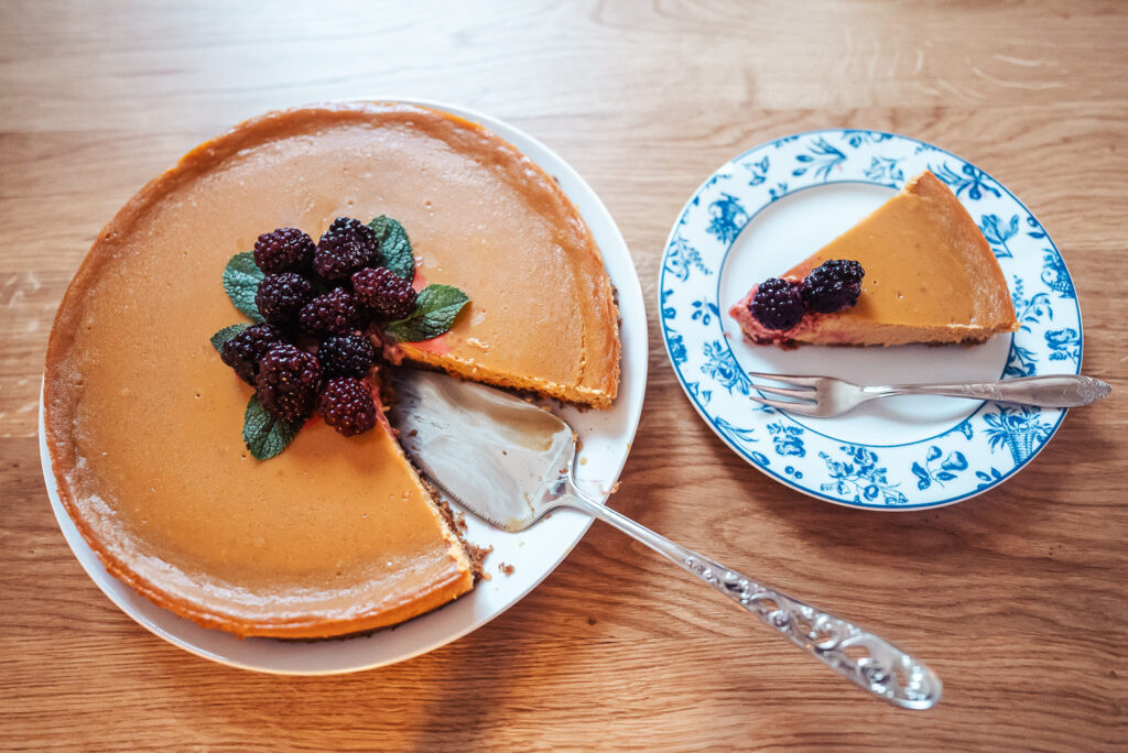 Norwegian brunost (brown cheese) cheesecake with blackberries and fresh mint on a counter with one slice on a plate