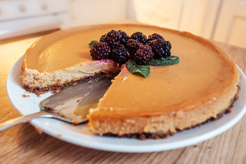 Norwegian brown cheese cheesecake topped with blackberries and fresh mint served on a plate with one slice removed