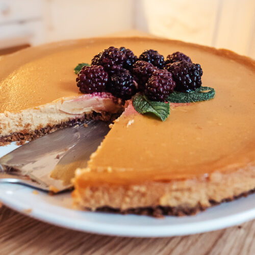 Norwegian brown cheese cheesecake topped with blackberries and fresh mint served on a plate with one slice removed