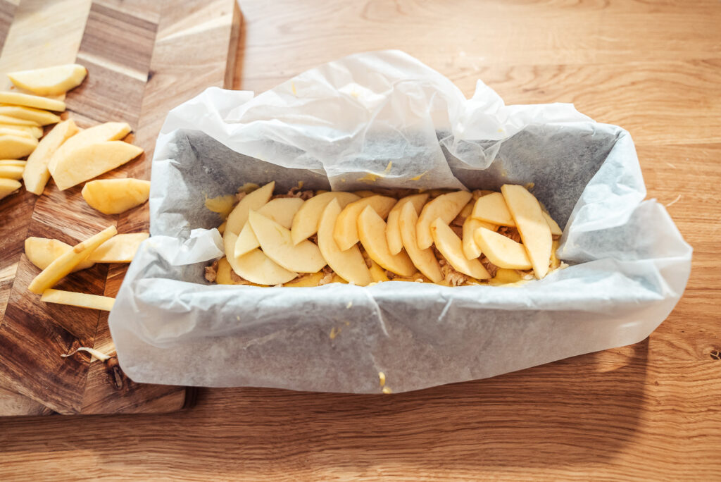 layering apples on top of Norwegian almond cake in a loaf pan